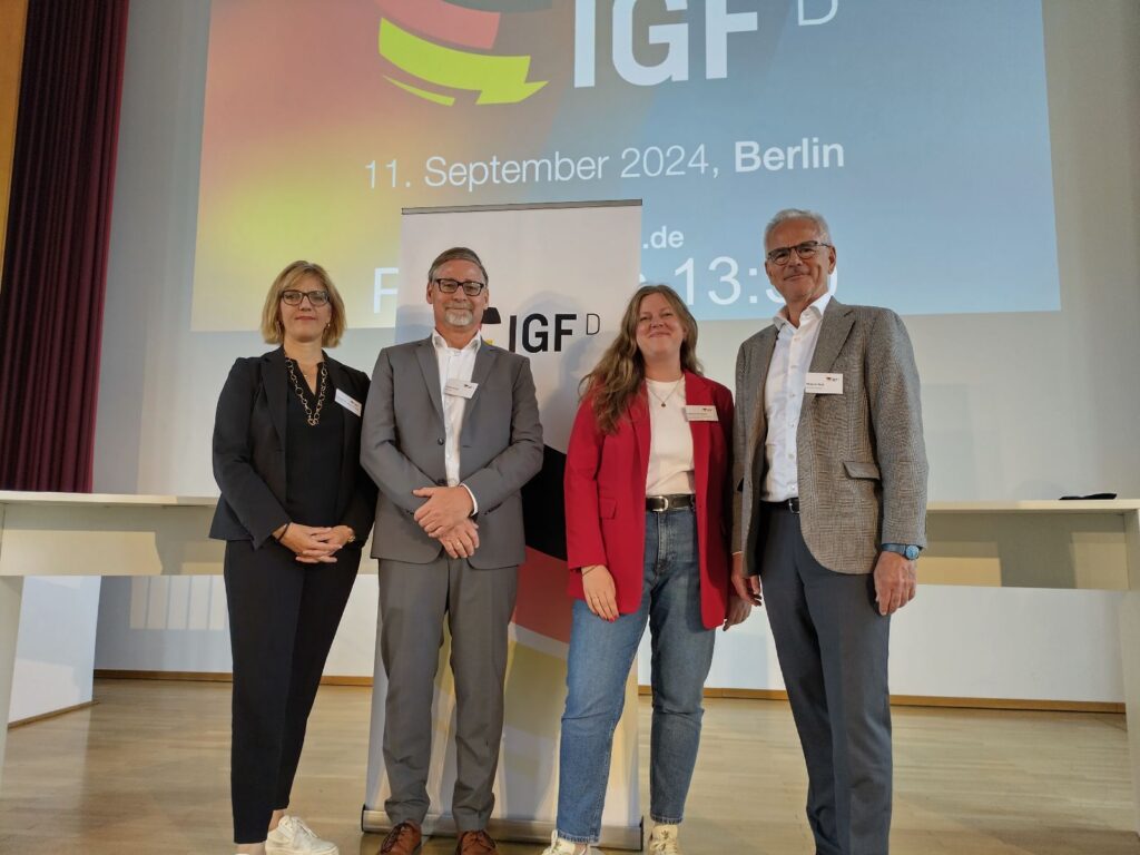 Vier Personen stehen vor einem Schild mit der Aufschrift „IGF“