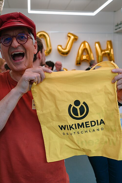 Ein Mann hält einen gelben Jutebeutel mit dem WIkimedia-Logo hoch