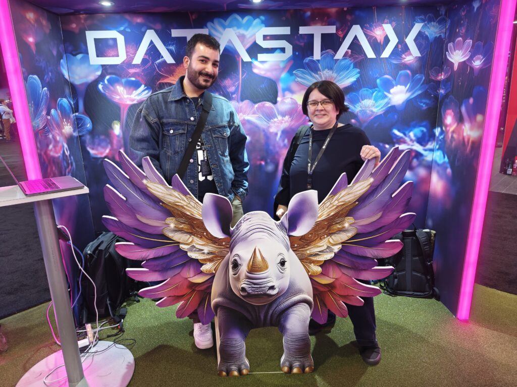 Lydia Pintscher und Philippe Saadé stehen vor einem Poster mit dem Datastax-Logo. Vor ihnen steht eine Nashorn-Figur mit Flügeln.