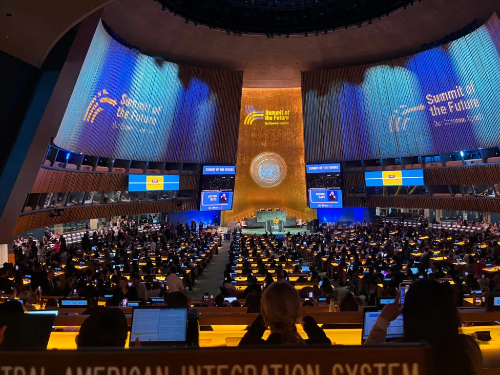 A large conference room. “Summit of the Future” is written on the walls.