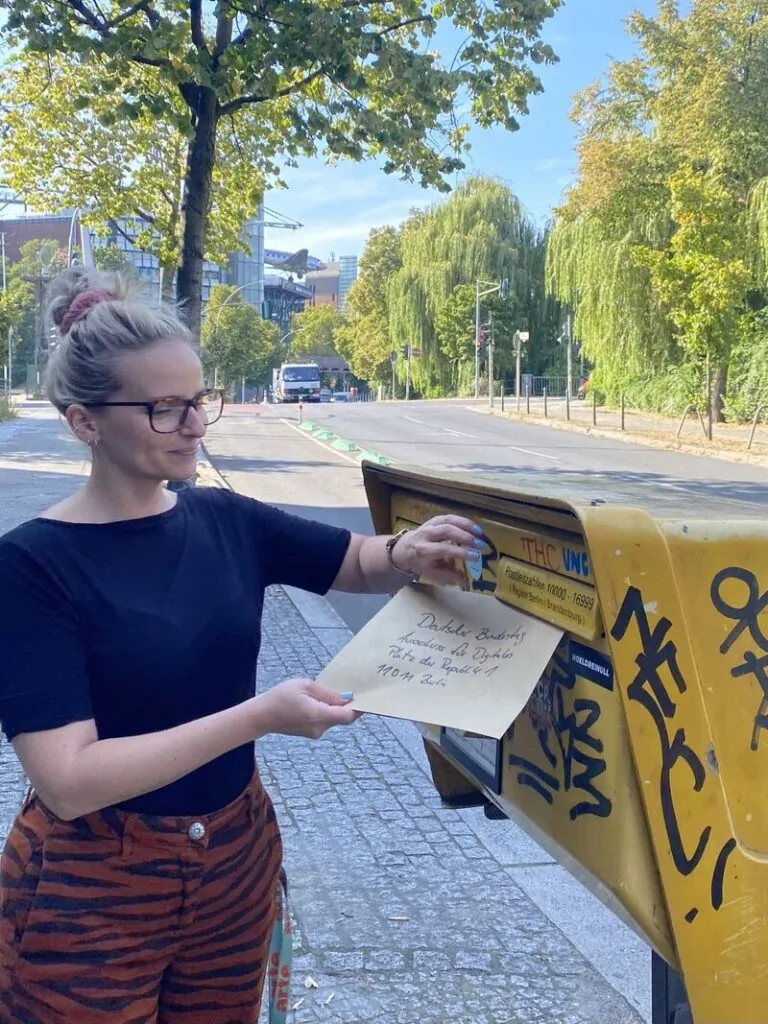 Eine Frau steckt einen großen Umschlag in einen Briefkasten.