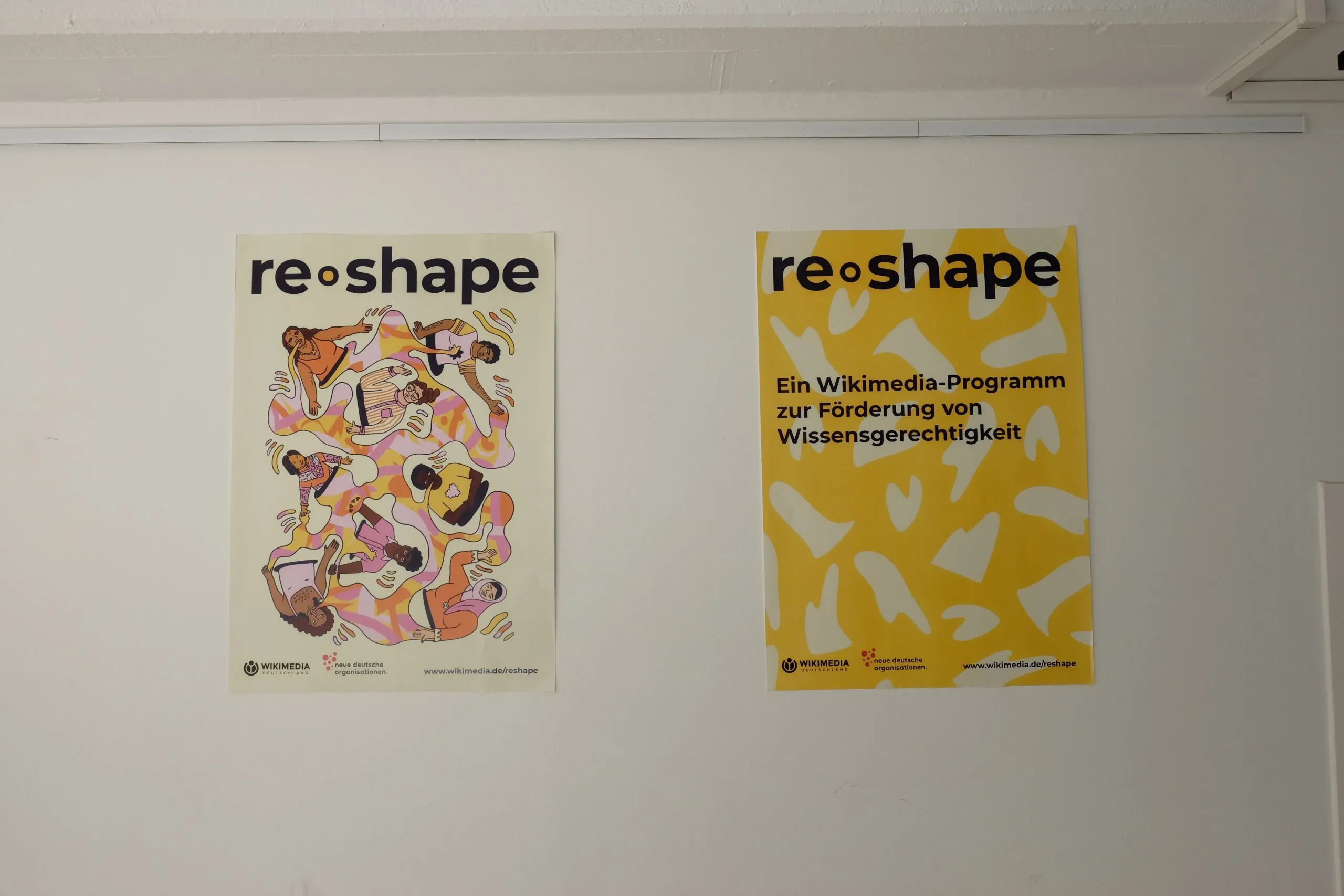 Zwei re-shape Poster hängen an einer weißen Wand.