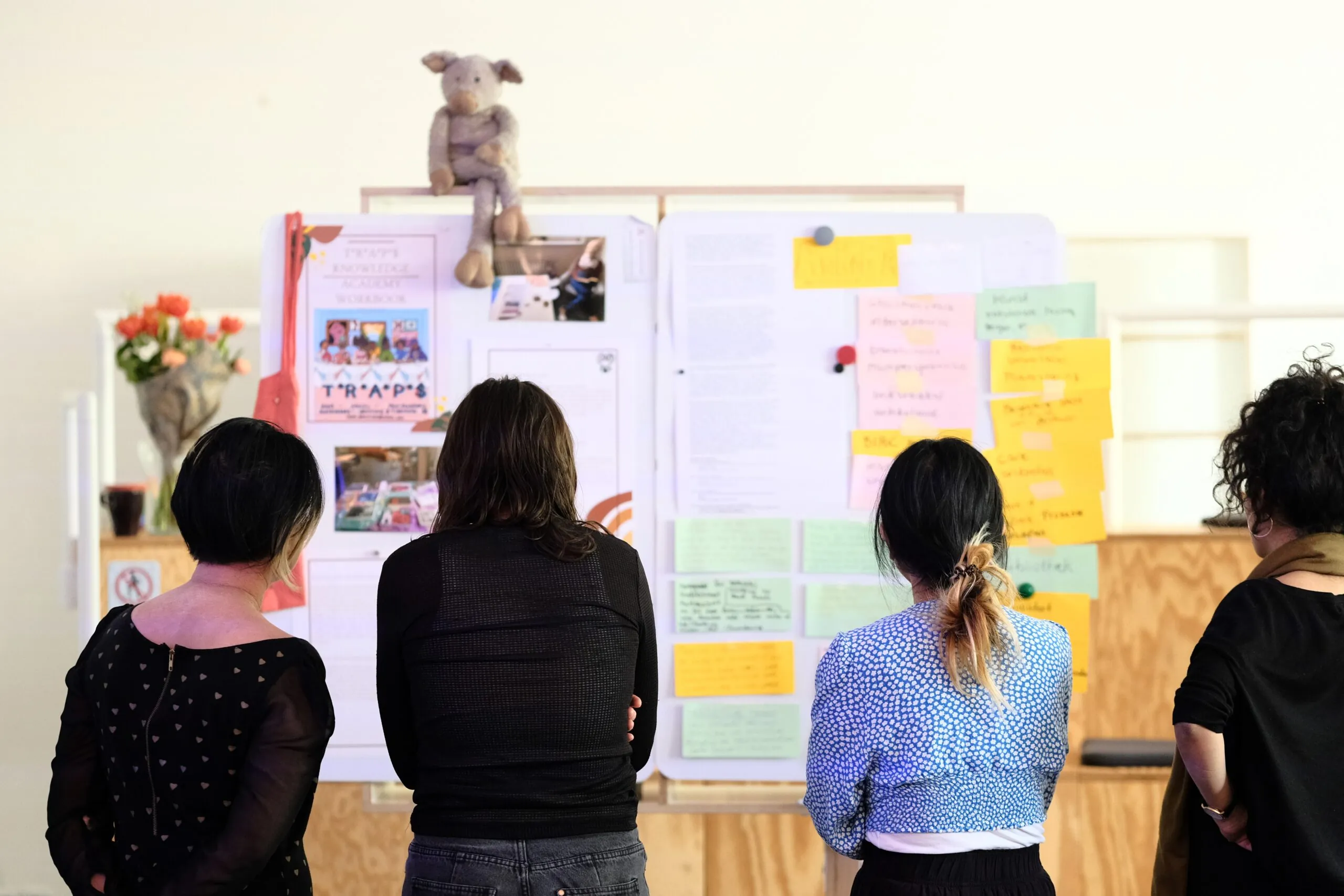 Four people stand with their backs to the camera and look at a whiteboard with colorful notes.