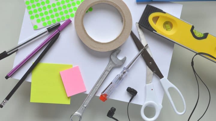 An assortment of tools used for work as well as building, including pens, scissors, post-its, sticker dots, and headphones, as well as mechanical tools such as a wrench, spirit level and screw driver.