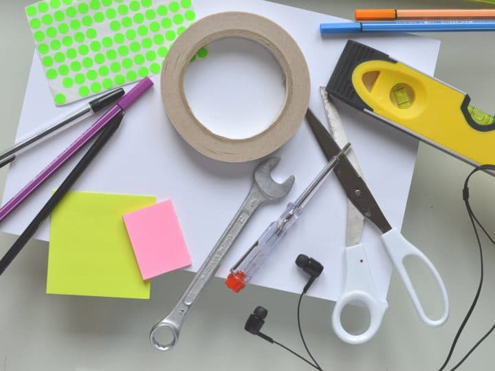 An assortment of tools used for work as well as building, including pens, scissors, post-its, sticker dots, and headphones, as well as mechanical tools such as a wrench, spirit level and screw driver.