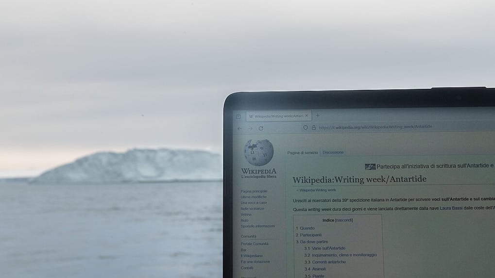 Laptop mit der Wikipedia-Oberfläche im Fokus. Im Hintergrund sieht man Wasser und einen Eisberg.