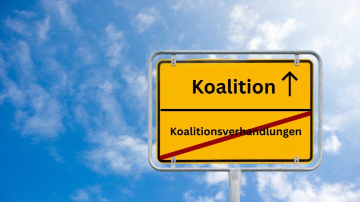 Das Bild zeigt einen blauen und leicht bewölkten Himmel. Prominent im Bild zu sehen ist ein typisch deutsches Ortseingangsschild in gelber Farbe. Auf dem unteren Teil steht das Wort Koalitionsverhandlungen. Es ist durchgestrichen. Im oberen Teil steht das Wort Koalition neben dem ein Pfeil zu sehen ist, der symbolisch in die Zukunft weist.
