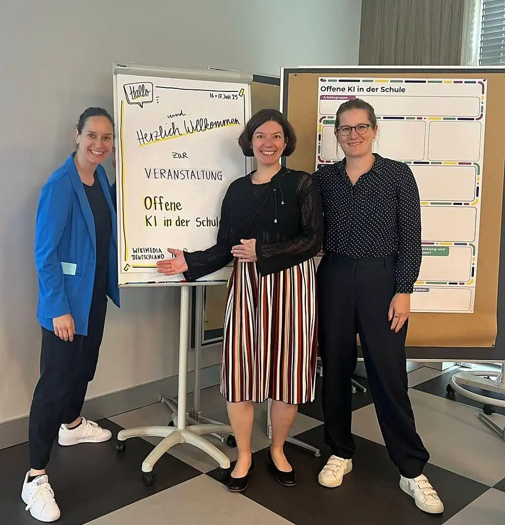 Sarah Behrens, Anne-Sophie Waag und Chirstine Oymann vor dem Begrüßungschart für die OKIS Tagung 2025